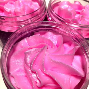 May include: Three glass jars filled with a pink whipped body butter. The body butter has a swirl design and a shimmery finish.