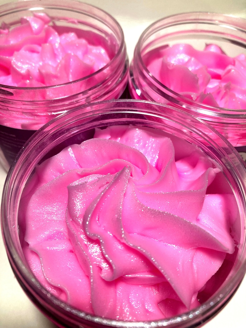 May include: Three glass jars filled with a pink whipped body butter. The body butter has a swirl design and a shimmery finish.
