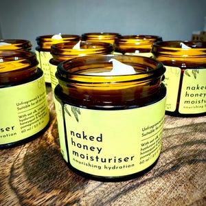May include: Multiple amber glass jars filled with white cream, each featuring a yellow label with black text that reads naked honey moisturiser nourishing hydration, 60 ml / 2.11 fl oz, unfragranced and suitable for all skin types.