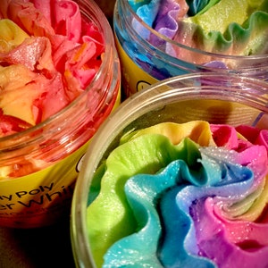 May include: Three glass jars filled with colorful whipped soap. The soap is swirled with shades of pink, blue, green, and yellow. The jars have labels that say "Whipped Body Butter" and "Soy Poly Whipped Body Butter".