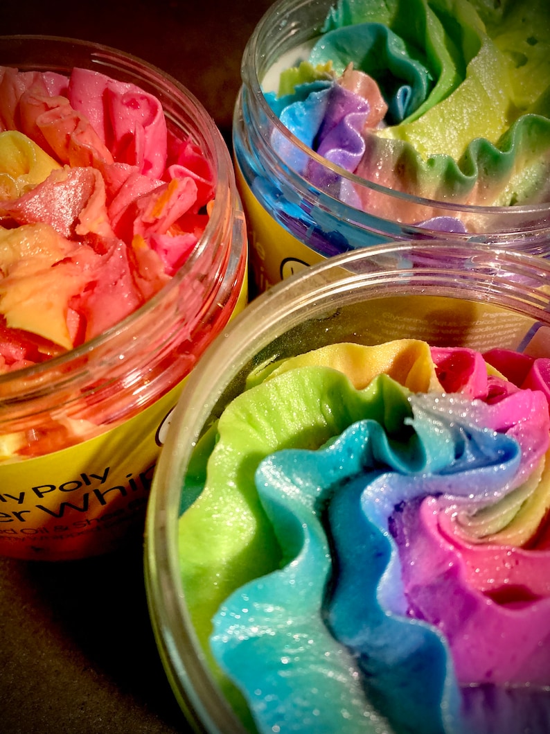 May include: Three glass jars filled with colorful whipped soap. The soap is swirled with shades of pink, blue, green, and yellow. The jars have labels that say "Whipped Body Butter" and "Soy Poly Whipped Body Butter".