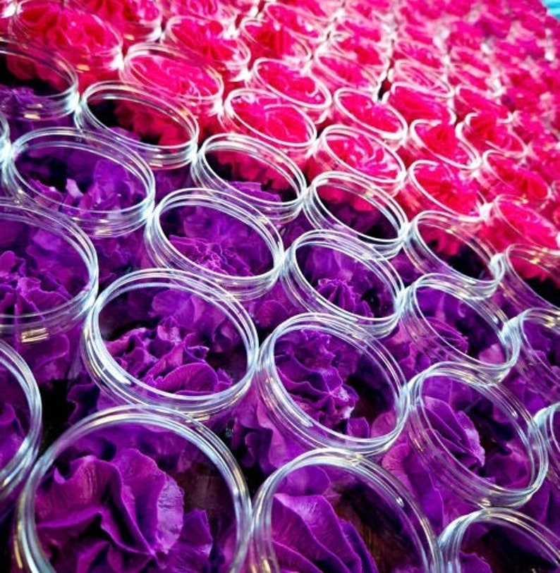 May include: Close-up of multiple clear glass jars filled with purple flowers. The jars are arranged in rows, creating a pattern of purple and clear.