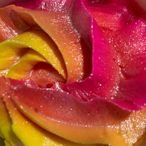 May include: Close-up of a swirl of pink, orange, and yellow frosting. The frosting has a sparkly, glittery texture.