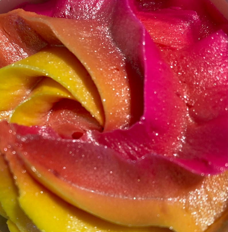 May include: Close-up of a swirl of pink, orange, and yellow frosting. The frosting has a sparkly, glittery texture.
