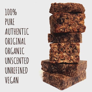 May include: A vertical stack of six rectangular, dark brown, textured blocks. To the left, the text reads: 100% PURE, AUTHENTIC, ORIGINAL, ORGANIC, UNSCENTED, UNREFINED, VEGAN. The blocks have a coarse, granular appearance with visible dark particles.