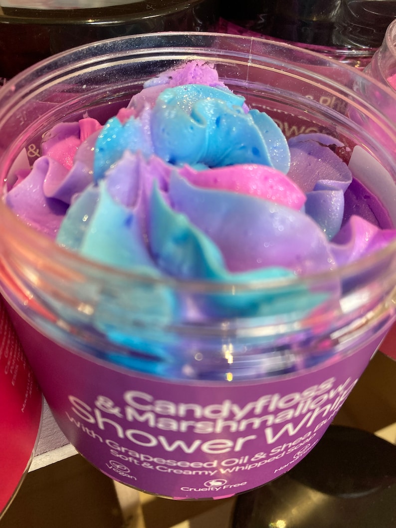 May include: A purple jar with a blue and pink swirl of whipped shower gel. The label reads "Candyfloss & Marshmallow Shower" with "Grapeseed Oil & Shea Butter Soft & Creamy Whipped Soap" in smaller text. The jar also has a vegan and cruelty-free logo.