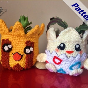 May include: Two crocheted Pokemon planter pots, one yellow with a brown stripe and a red tongue, the other white with red, blue, and white accents. Both pots have large eyes and are filled with small plants.