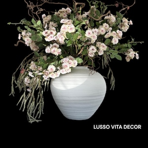 Może przedstawiać: Biały, teksturowany wazon wypełniony różowymi i białymi różami, zielonymi liśćmi i brązowymi gałęziami. Kompozycja jest ustawiona na czarnym tle. Tekst "LUSSO VITA DECOR" znajduje się na dole.