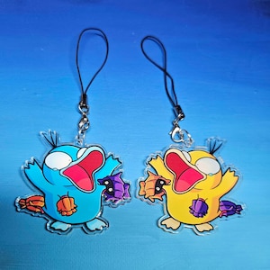May include: Two cartoon character keychains, one blue and one yellow, with black eyes and open mouths. Both characters are holding purple and orange objects in their hands.
