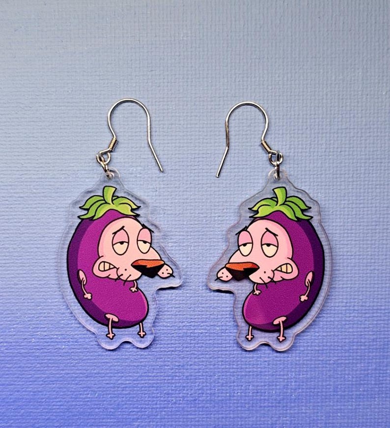 May include: A pair of dangle earrings featuring a cartoon character design. Each earring is shaped like a purple eggplant with a green leafy top and a cartoon dog face. The earrings have silver-colored fish hook ear wires.