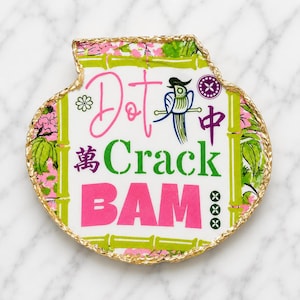 Puede incluir: Una bandeja decorativa con forma de concha y borde pintado en oro. El centro presenta el texto Dot, Crack y BAM en rosa y verde, junto a una ilustraci&oacute;n de un p&aacute;jaro azul, tallos de bamb&uacute; verdes, motivos florales rosas y caracteres chinos.