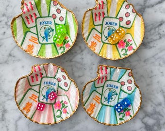 May include: Four scalloped shell-shaped dishes with gold-painted edges, each featuring a central Joker playing card graphic with a blue bird, surrounded by Mahjong tile motifs, pink flowers, and translucent colored dice in green, yellow, red, and blue.