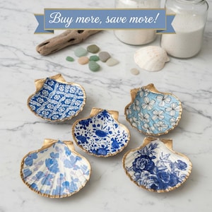 May include: Six decorative seashell dishes with gold rims and blue and white floral patterns. The text "Buy more, save more!" is displayed above the shells. The shells are arranged on a marble surface.