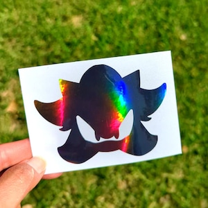 May include: A black and iridescent vinyl sticker of Shadow the Hedgehog's head. The sticker is on a white background.