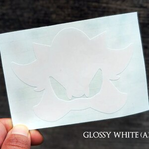 May include: White vinyl sticker with a silhouette of a cartoon character with a menacing expression. The character has a large head with sharp teeth and a pointed nose. The sticker is on a white background.