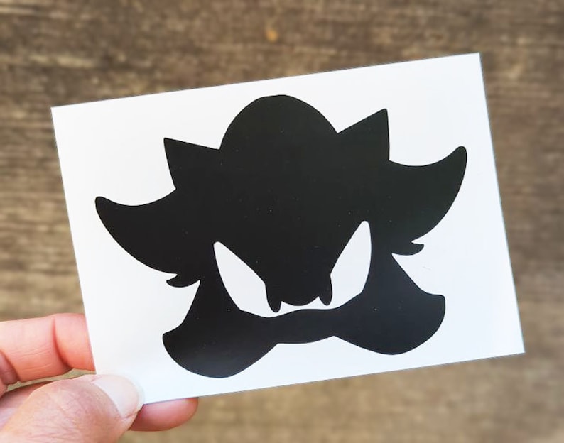 May include: Black silhouette of a cartoon character with sharp teeth and a spiky head. The character is facing forward with its mouth open.