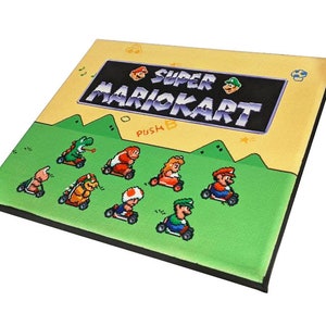 May include: A canvas print featuring the Super Mario Kart video game title card. The image shows a yellow background with the text "SUPER MARIOKART" in a black box with purple lettering. The text "PUSH B" is visible below the title. The image also shows eight characters from the game racing on a green track.