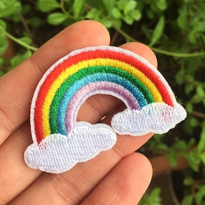 May include: Embroidered rainbow patch with red, orange, yellow, green, blue, and purple arches. The rainbow is bordered by white clouds. The patch is designed for application on clothing or accessories.