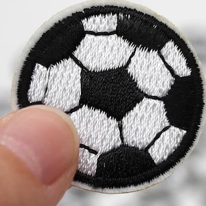 Op de afbeelding: Geborduurde patch met een voetbalontwerp. De patch heeft een zwart-wit kleurenschema, met de vijfhoekige en zeshoekige vormen van de voetbal duidelijk gedefinieerd. De patch is rond met een witte rand.