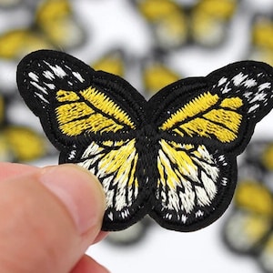 May include: Embroidered butterfly patch with black, yellow, and white details. The butterfly has a black outline and detailed wing patterns. The patch is likely for clothing or accessories.