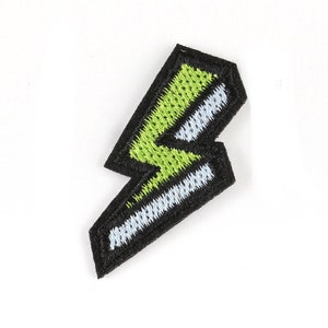 May include: Embroidered patch in the shape of a lightning bolt. The patch features a black border, with a green and white lightning bolt design. The patch is likely for clothing or accessories.