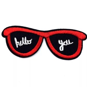 Peut inclure: Écusson brodé représentant des lunettes de soleil avec des montures rouges et des verres noirs. Les mots "hello you" sont brodés en blanc sur les verres. Pour vêtements ou accessoires.