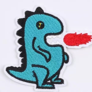May include: Embroidered patch featuring a cartoon dinosaur in teal with black accents and a red flame. The dinosaur has a white border and is smiling. The patch is designed for application on clothing or accessories.