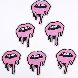 May include: A collection of seven pink lip-shaped patches with black outlines and dripping details. The patches feature open mouths with white teeth. These embroidered patches are ideal for adding a unique touch to clothing or accessories.