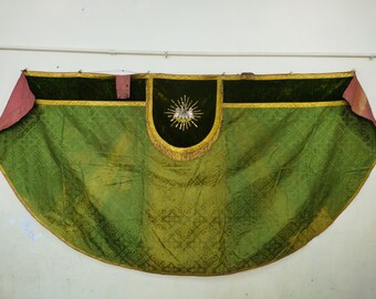May include: A green and gold ceremonial textile with a central dark green panel featuring an emblem. The textile has a patterned design and is trimmed with gold and fringe. Pink fabric accents the corners.