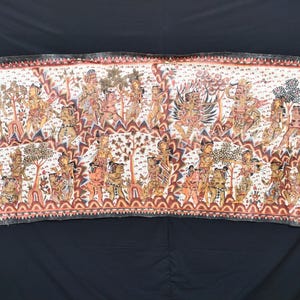 Puede incluir: Textil rectangular pintado a mano que presenta una escena detallada con numerosas figuras, árboles y elementos arquitectónicos. La obra de arte utiliza una paleta de colores cálidos con rojos, marrones y tonos tostados, sobre un fondo blanco con un borde estampado.
