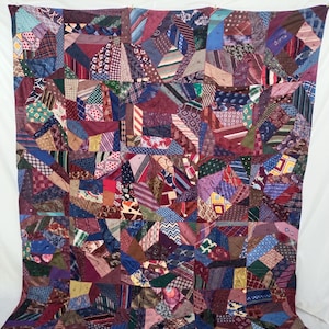 Puede incluir: Una colcha construida a partir de un mosaico de varias corbatas que presenta una amplia gama de colores, incluidos rojos profundos, azules, morados y verdes, junto con diversos patrones como rayas, lunares, cachemira y formas geométricas.