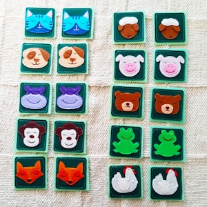 May include: A set of 18 felt squares with different animal faces. The squares are green with white stitching around the edges. The animals include a cat, dog, hippopotamus, monkey, frog, fox, chicken, and bear.