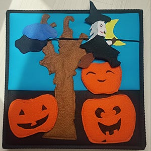 May include: A felt Halloween square with a blue sky backdrop, a brown tree, and two orange pumpkins with smiling faces. A witch on a broom and a crescent moon are also depicted.