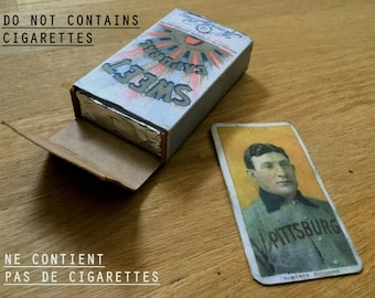 May include: A vintage box of Sweet Caporal cigarettes with a silver foil lining. The box is open and the text "DO NOT CONTAINS CIGARETTES" is visible on the front. The text "NE CONTIENT PAS DE CIGARETTES" is visible on the bottom of the box. A baseball card with a picture of a man in a Pittsburgh uniform is visible in the background.