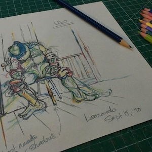 May include: A colored pencil sketch on white paper depicting a seated turtle character wearing a blue mask. The drawing includes the text Leo, Leonardo Sept 19, '90, and a handwritten note stating needs shadows. A blue pencil and a stack of colored pencils are visible.