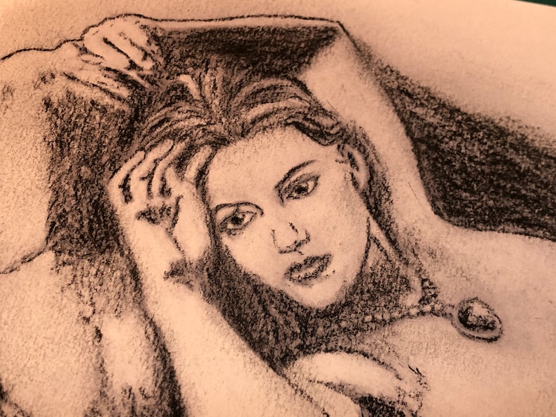 May include: A black and white charcoal drawing of a woman with long hair, wearing a necklace with a large gemstone pendant. The woman is lying down with her head resting on her hand.