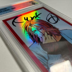 Può includere: Una carta collezionabile valutata con un'immagine olografica di Kurt Cobain. La carta ha un bordo rosso e una custodia protettiva trasparente. Il nome "Kurt" è scritto in nero.