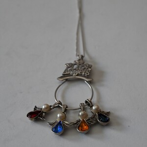 May include: A silver necklace with a charm that says "Our Angels" and four dangling angel charms with red, blue, orange, and white gemstones.