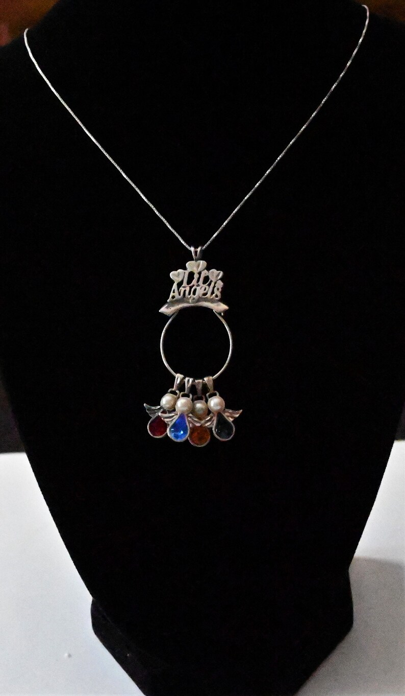May include: Silver necklace with a pendant that says "My Angels" with a circle and five angel charms with coloured stones.