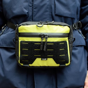 May include: A black and yellow fanny pack with a zipper and a black velcro panel with the text "TLSB".
