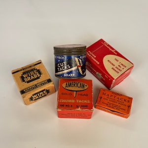 May include: Assortment of vintage boxes of tacks and brads. The boxes are red, orange, and brown with white lettering. The boxes contain 1 inch round head brass tacks, solid head thumb tacks, and wire brads.
