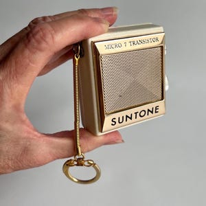 May include: A vintage white and gold SunTone Micro 7 Transistor radio with a gold chain and a key ring. The radio has a speaker grille and the text "MICRO 7 TRANSISTOR" and "SUNTONE" printed on the front.
