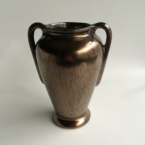 May include: A bronze-colored ceramic vase with two handles. The vase has a textured surface and a rounded base.