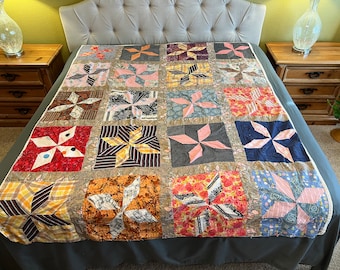 May include: A patchwork quilt with a variety of fabrics and colors, including red, pink, blue, and yellow. The quilt is made up of squares with a star design in the center of each square. The quilt is on a bed with a gray headboard.