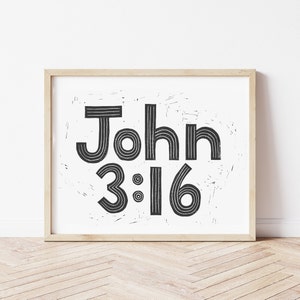 Könnte beinhalten: Schwarz-weiß Druck des Bibelverses Johannes 3:16 in einem Holzrahmen. Der Text ist in einer fetten, klobigen Schrift.