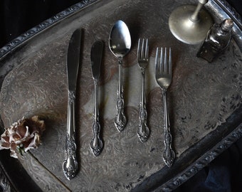Può includere: Un vassoio da portata d'argento con un motivo floreale decorativo, che comprende un coltello, un coltello da burro, un cucchiaio e due forchette.