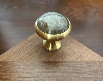 May include: A brass cabinet knob with a round, light gray stone top. The stone has a swirling pattern.
