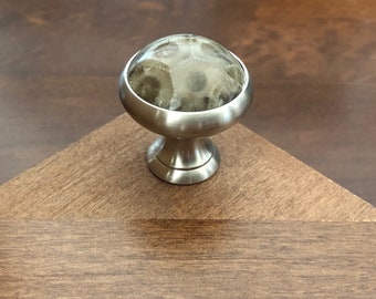 May include: A silver cabinet knob with a round, light brown, fossilized stone top.