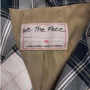 May include: Close-up of a plaid blazer with a label that reads "We The Free." The label also indicates the size is XL and the garment was made in Cambodia. The blazer features a green, white, and pink plaid pattern.