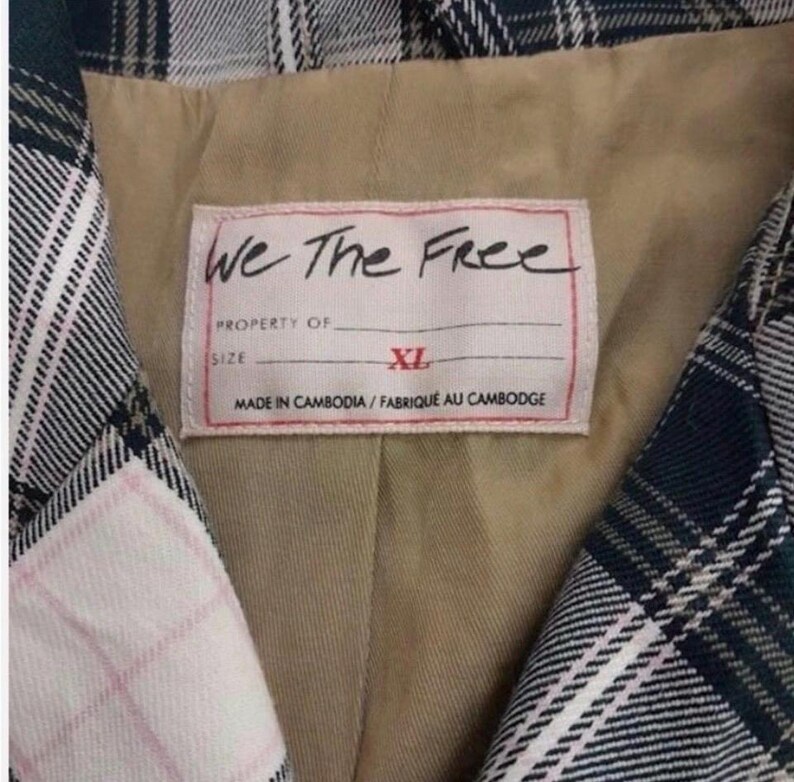 May include: Close-up of a plaid blazer with a label that reads "We The Free." The label also indicates the size is XL and the garment was made in Cambodia. The blazer features a green, white, and pink plaid pattern.